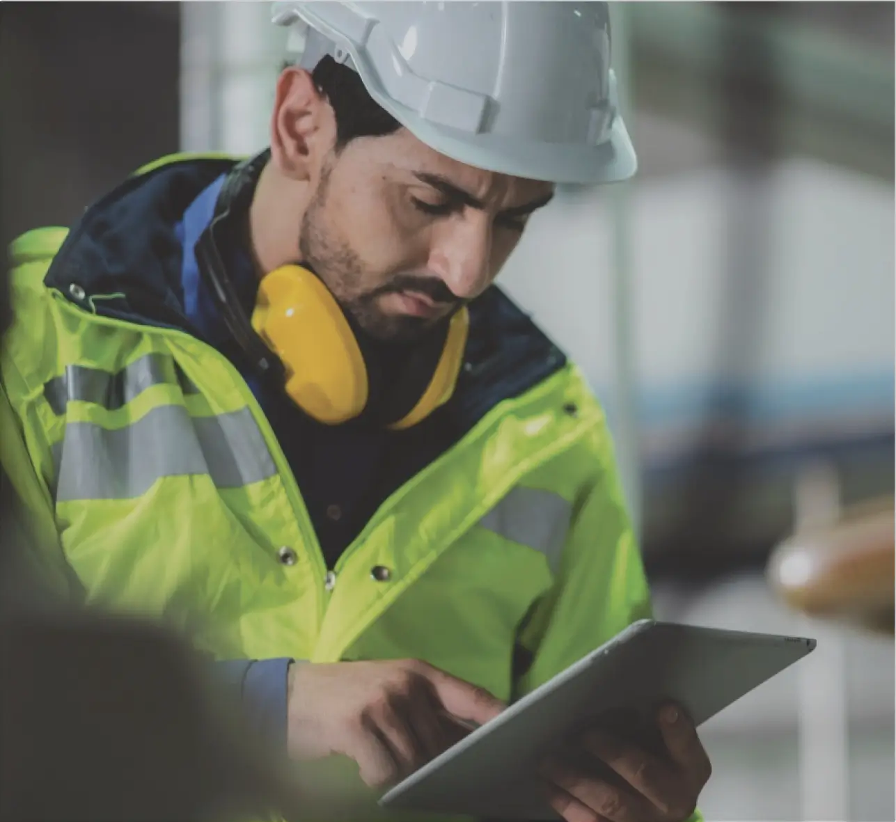 A worker in a hard hat and hi-vis jacket using a tablet